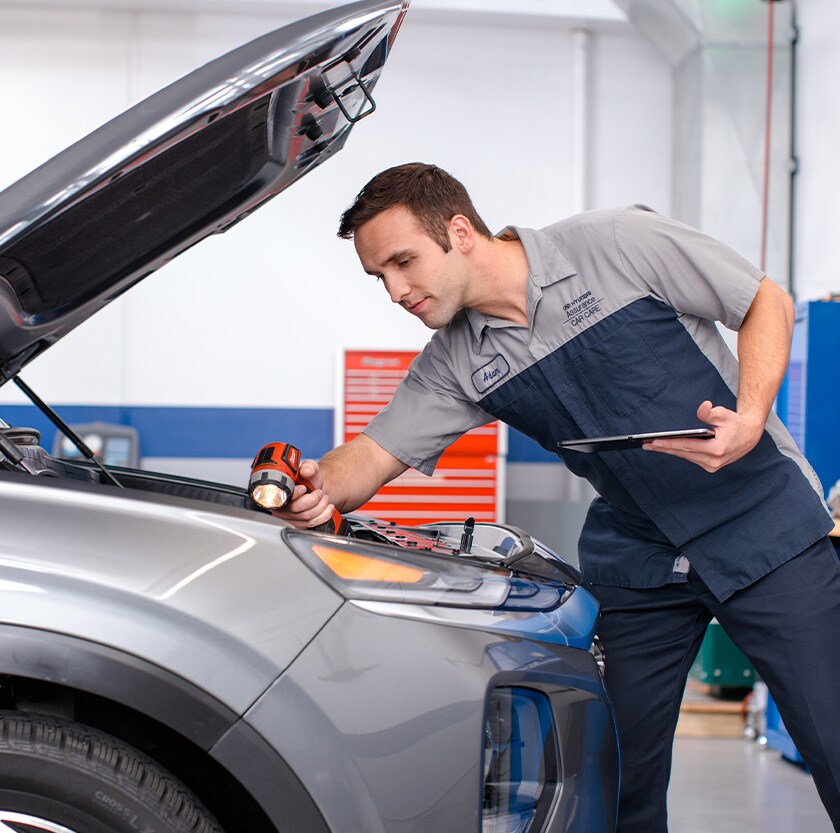 Everything You Need to Know about Your Car Battery at West Broad Hyundai | Hyundai Service Advisor Checking Under Hood of Hyundai Vehicle with Flashlight
