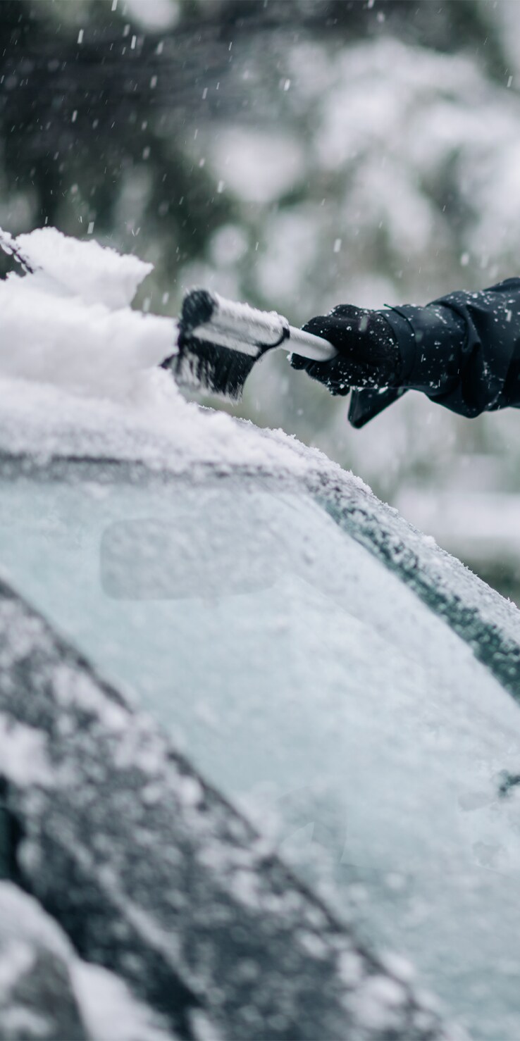 How to Prevent your Vehicle from Fogging Up At West Broad Hyundai in Henrico, VA | Persons hand with black gloves is using a cleaning brush to wipe of snow from windshield
