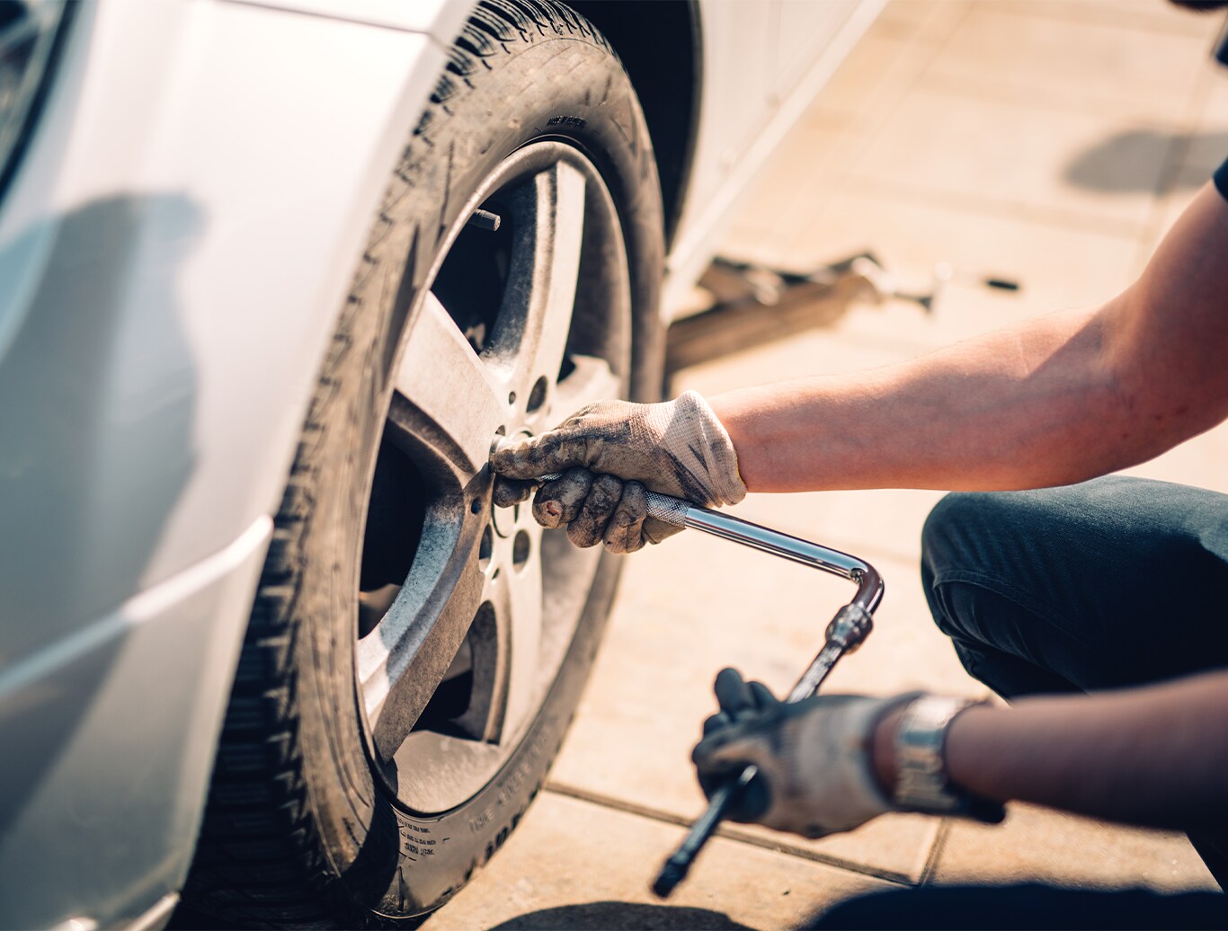 What is Tire and Rim Protection? | West Broad Hyundai | Person with dirty white gloves is using a socket tool to remove wheel lug nuts on a silver car