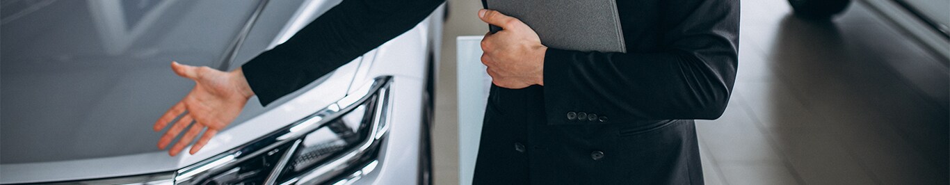 Enjoy A Test Drive At West Broad Hyundai in Henrico, VA | Man in black suit is holding a clipboard and showing a grey car on the left
