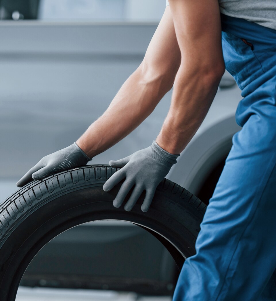 What is a Tire Rotation? at West Broad Hyundai | Photograph of a Male Car Technician Rolling a Tire Along the Floor