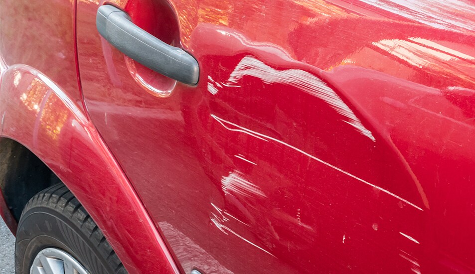 What is Paintless Dent Repair? | West Broad Kia | Red car with huge dent on side door with scratches