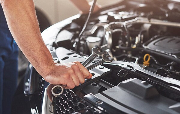 Basic Car Maintenance and Servicing Checklist | West Broad Kia | Car Technician Leaning Over Hood with Tools in Hand