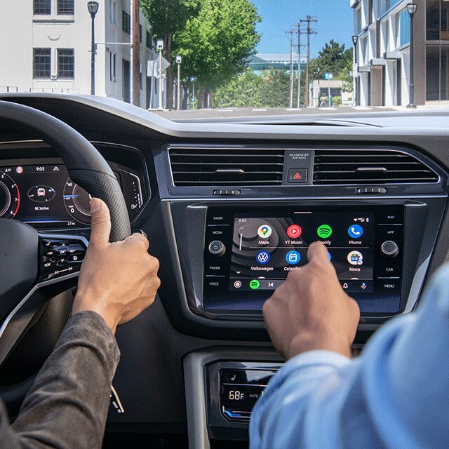 Things to Check When Buying a Used Car | West Broad Volkswagen in Richmond, VA | Hand From Passenger Seat Touching Apps on Center Console of 2022 Volkswagen Tiguan while Another Set of Hands Grasps the Sterring Wheel