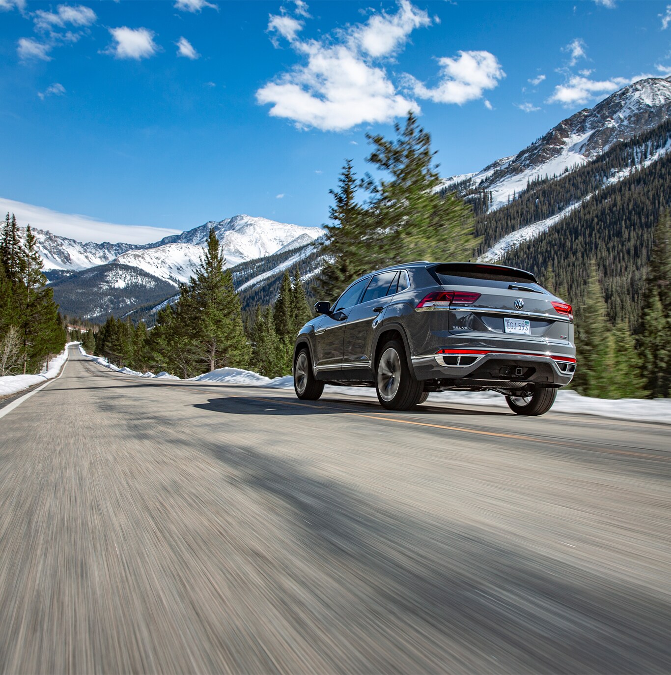 Model Features of the 2022 Volkswagen Atlas at West Broad Volkswagen | Rear view of a Matte Grey Volkswagen Atlas driving on the road with mountains and tall trees in the background