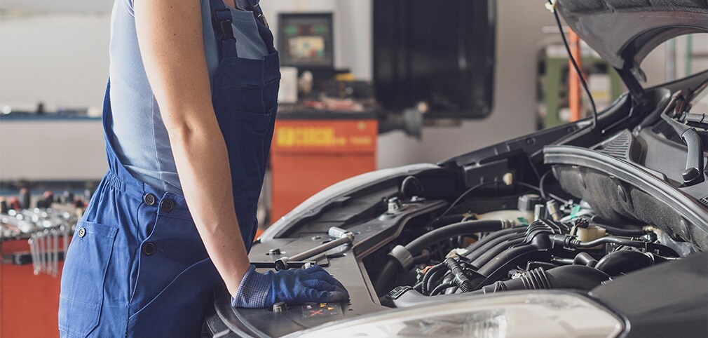 Learn Maintenance Warning Signs at West Broad VW in Richmond, VA | Mechanic in navy blue uniform with gloves is inspection the car engine with the hood open