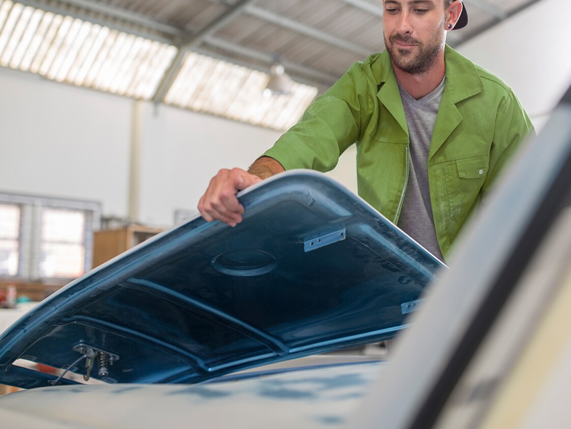 What is Paintless Dent Repair? | West Broad VW | Man in green shirt lifting a blue car panel