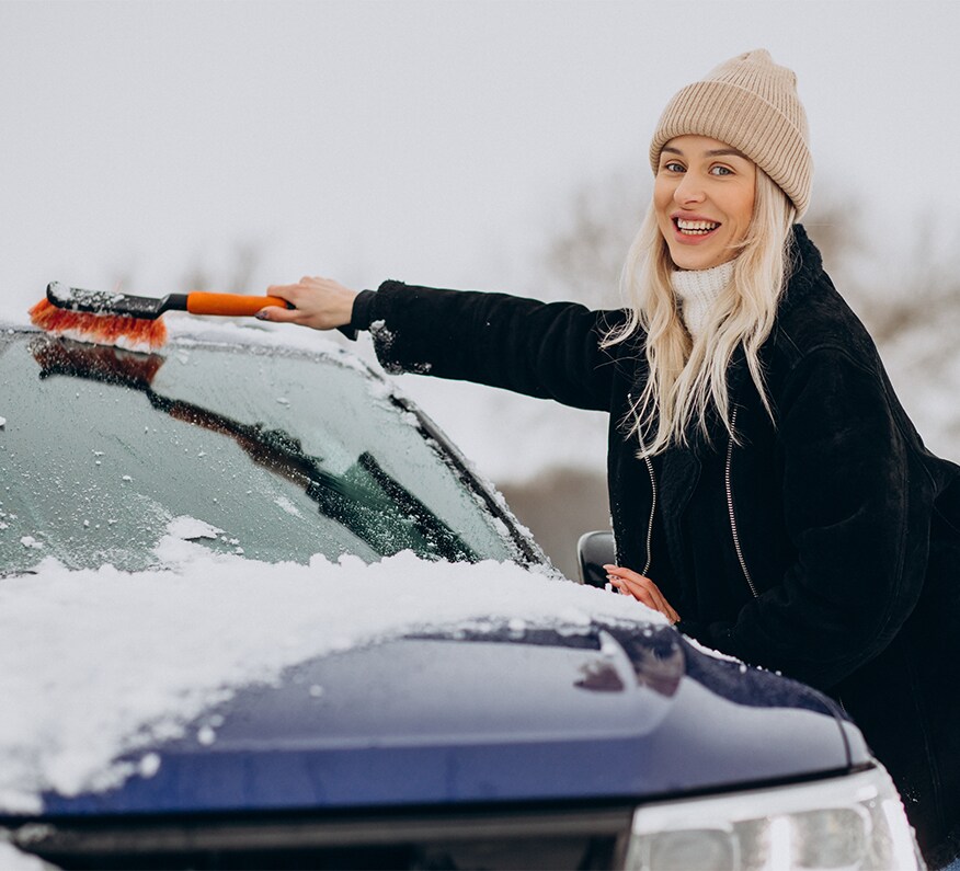 How to Prevent your Vehicle from Fogging Up At West Broad VW in Richmond, VA | Woman in black jacket is cleaning the windshield of her car by using a orange brush