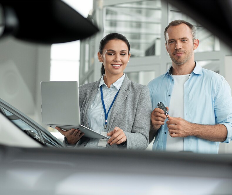 Enjoy A Test Drive At West Broad VW in Richmond, VA | Man in blue shirt on the right is looking at a car with a sales person on the left side holding a clipboard
