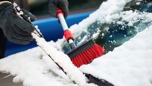 How to prepare your Volkswagen for the winter season in Richmond, VA at West Broad VW | Person using a red cleaning brush to scrape off snow from windshield