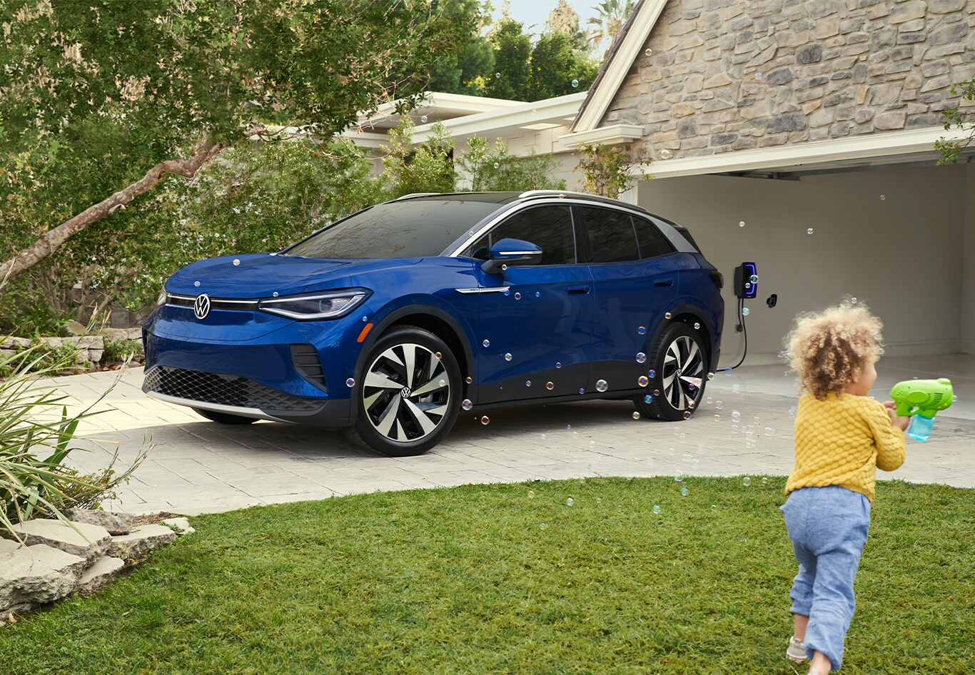 Android Auto vs. Apple CarPlay at West Broad VW in Richmond, VA | Blue 2023 Volkswagen ID.4 parked on house drive way while a little kid in yellow is playing with a bubble toy