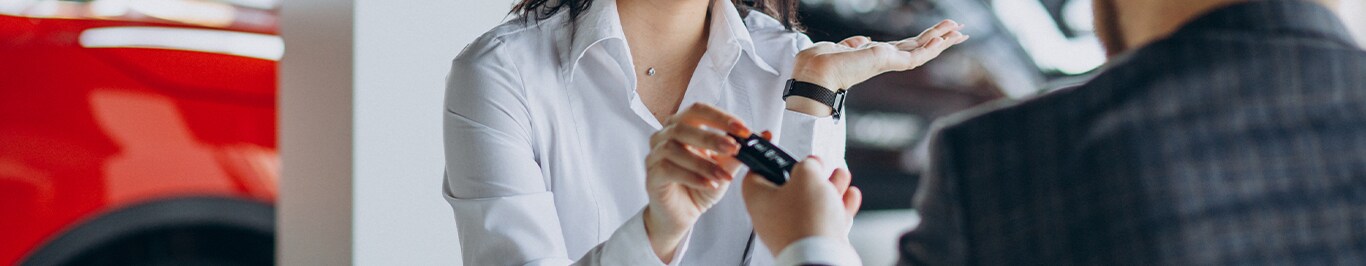 Enjoy A Test Drive At West Broad VW in Richmond, VA | Sales person handing over new car keys to a woman in a white shirt while there is a red car behind her