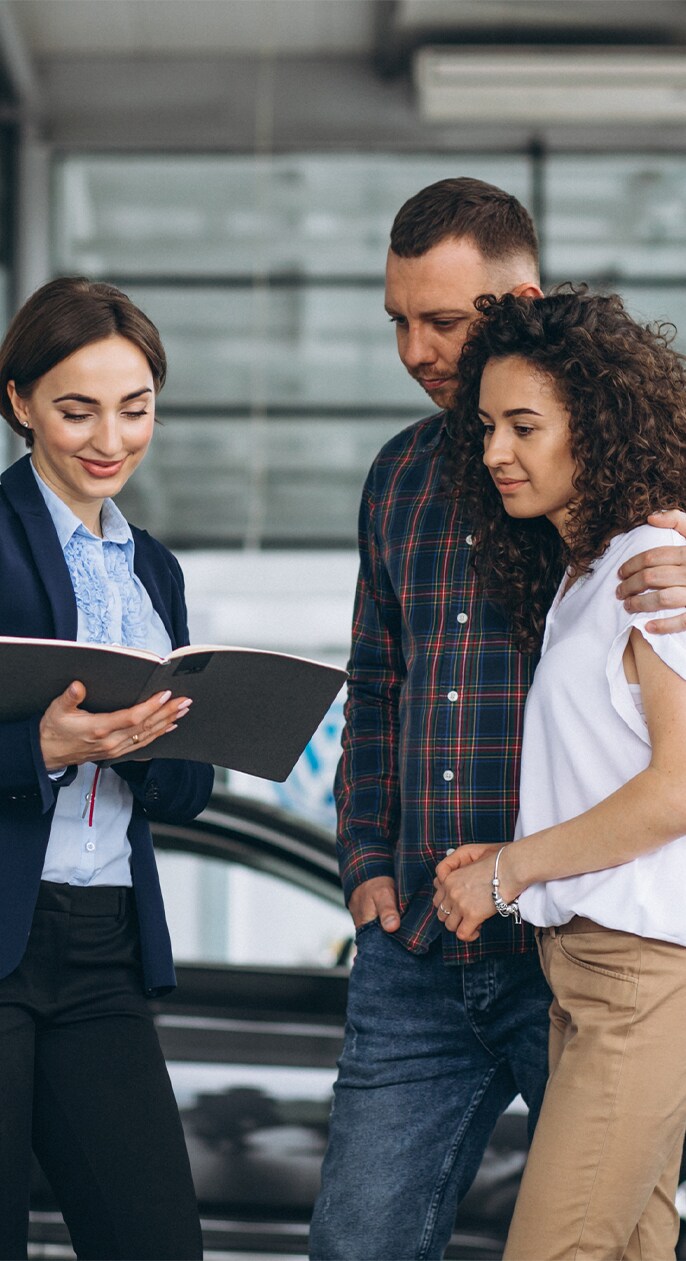 When to Trade In Your Car | West Broad VW in Richmond, VA | Salesperson on the left side is showing a open folder with documents to a couple on the right side at the dealership