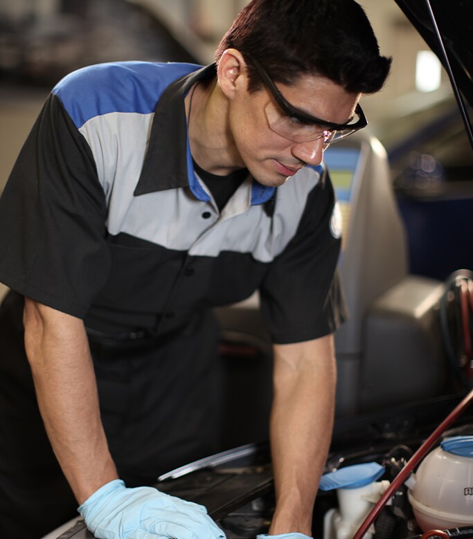 Best MPG At West Broad VW in Richmond, VA | Mechanic in black and grey uniform is wearing safety glasses and gloves to inspect car engine bay