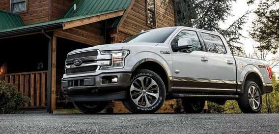 Test Drive With Us Today! A silver 2018 Ford F-150 parked near a cabin