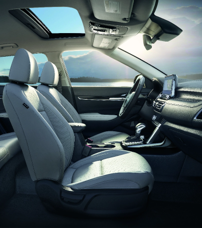 Modern SUV interior with light gray leather seats, panoramic sunroof, and center console, parked beside a lake with mountains visible through the windows.
