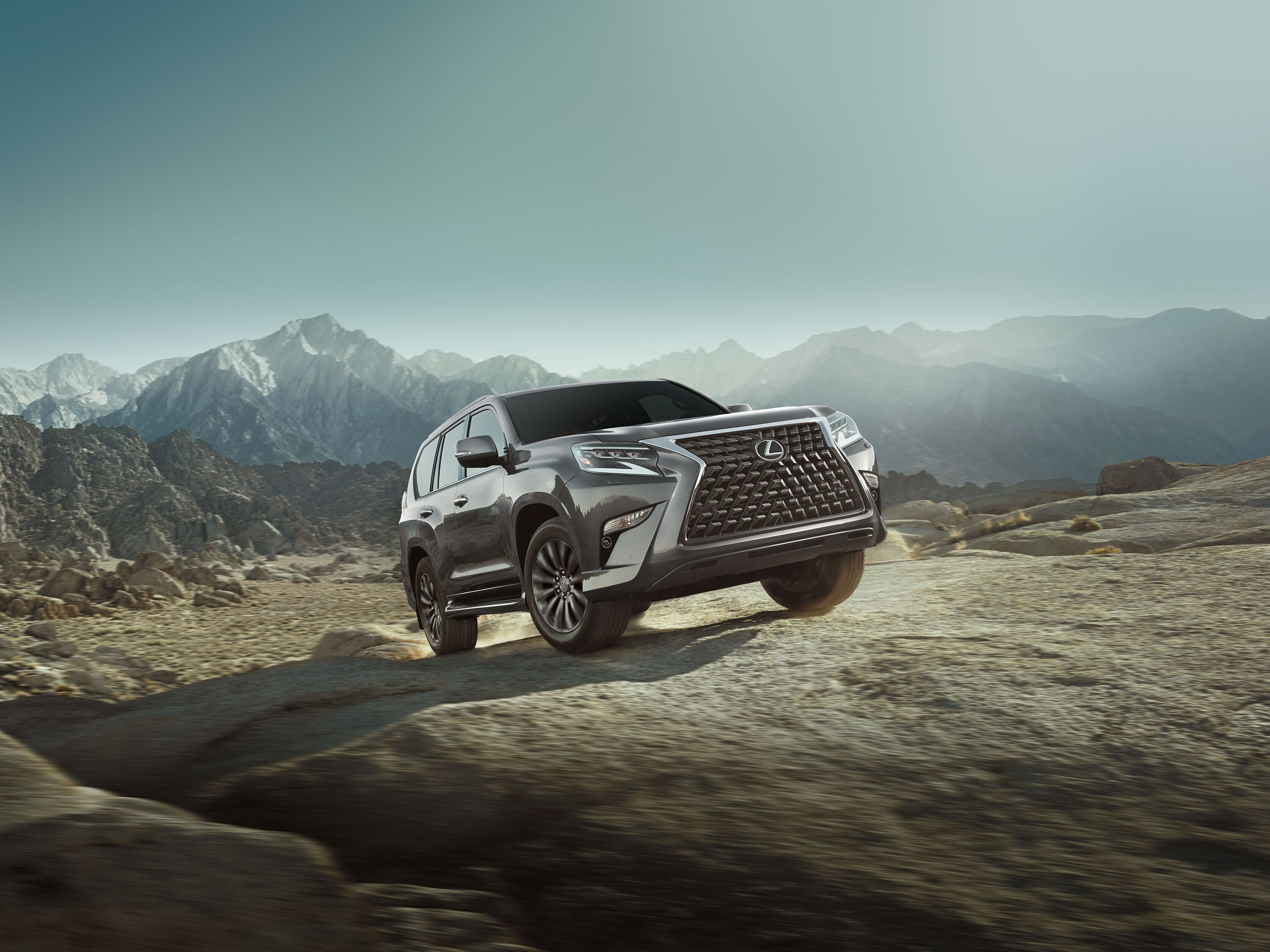Which Lexus is right for me? Gray Lexus GX luxury SUV navigating rugged off-road rocky terrain with mountain peaks in the background.
