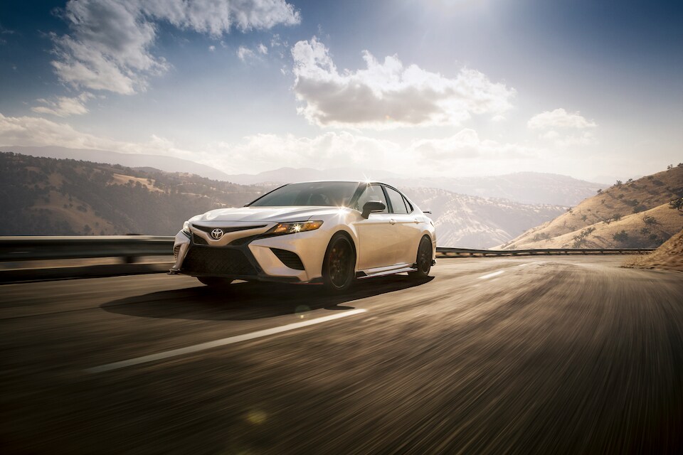 2020 Toyota Camry TRD Sedan driving on curving road against sky and clouds.jpeg