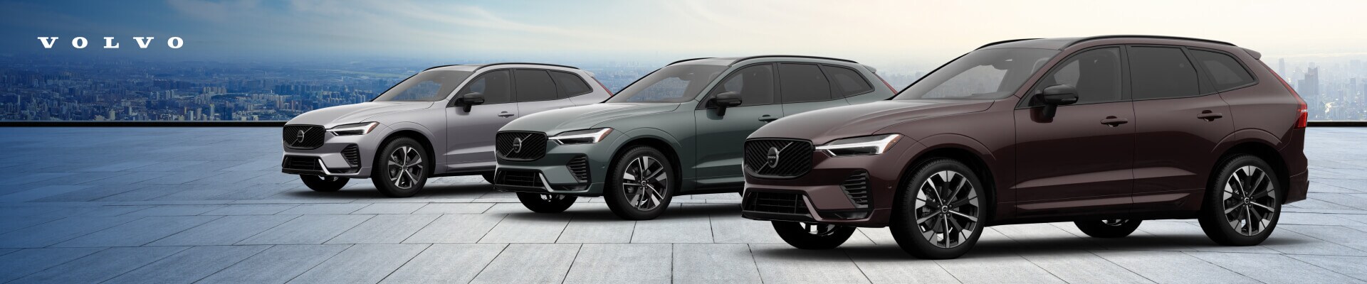 2026 Volvo XC60 Core in Aurora Silver, Plus in Forest Lake and Ultra in Mulberry Red against a city skyline.
