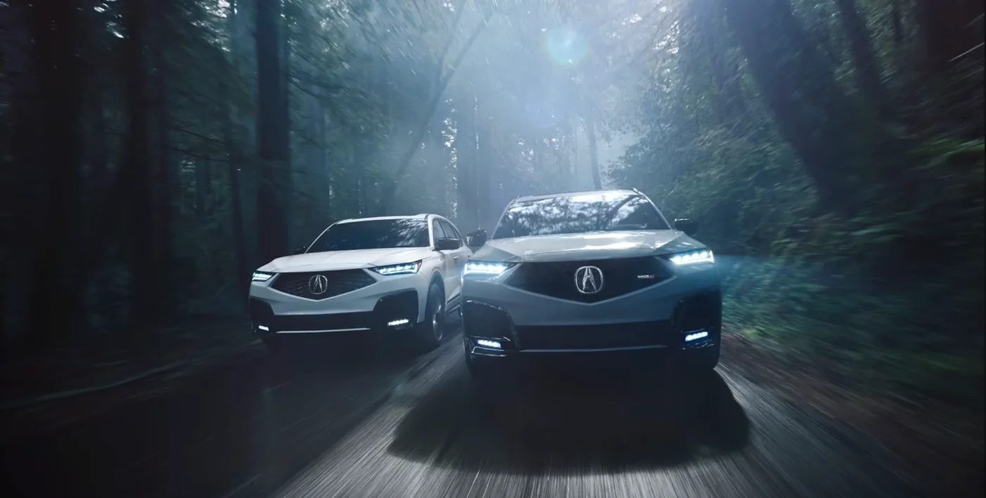 Two Acura MDX SUVs driving through a wooded road
