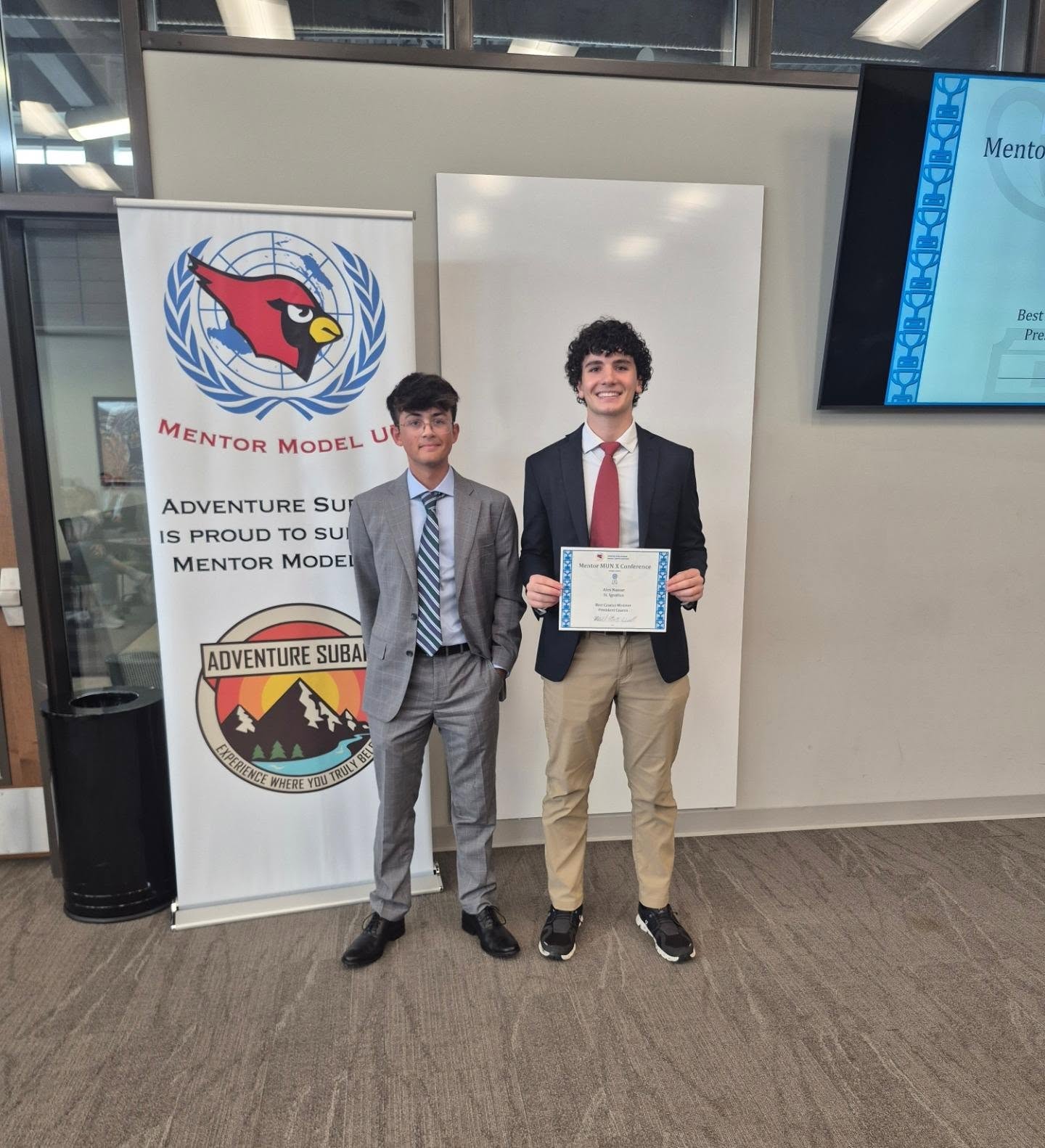 Two Mentor Model UN students, one holding an award certificate, beside the banner reading Adventure Subaru is proud to support Mentor Model UN.