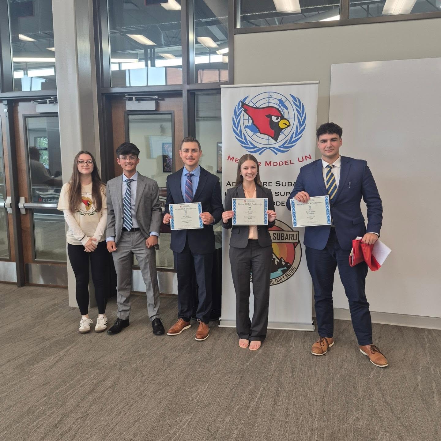 Five Mentor Model UN students, four holding award certificates, at Mentor MUN X in the Paradigm building at Mentor High School.