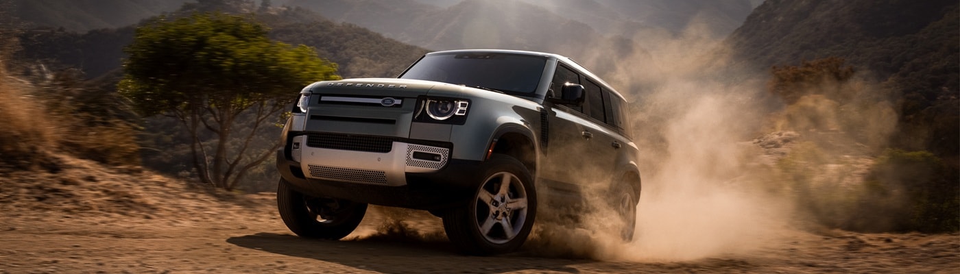 Defender 110 driving up a dusty hill on a sunny day