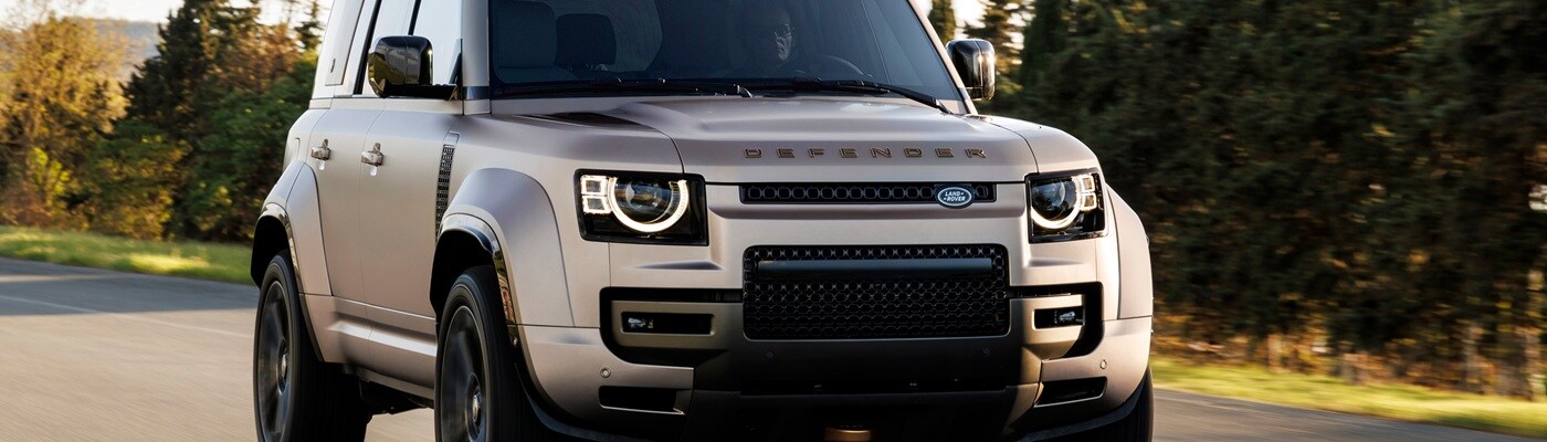 Front end of a Defender 130 driving on a road in the forest