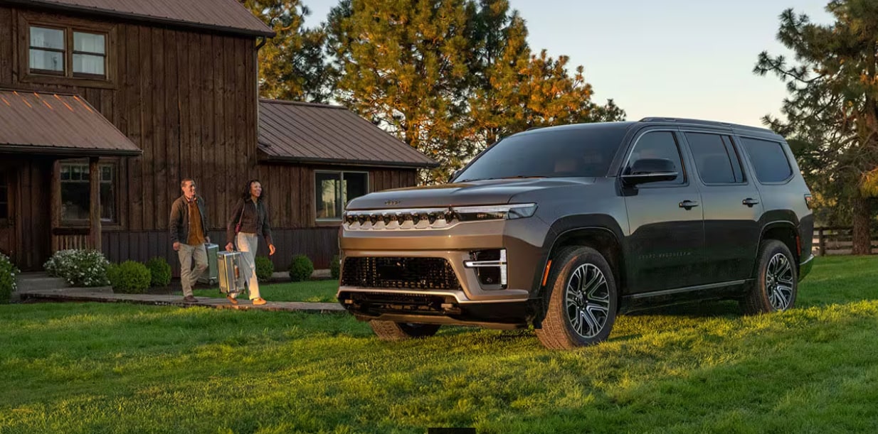 2026 Jeep® Grand Wagoneer parked on grass outside of cabin home with couple walking towards vehicle.