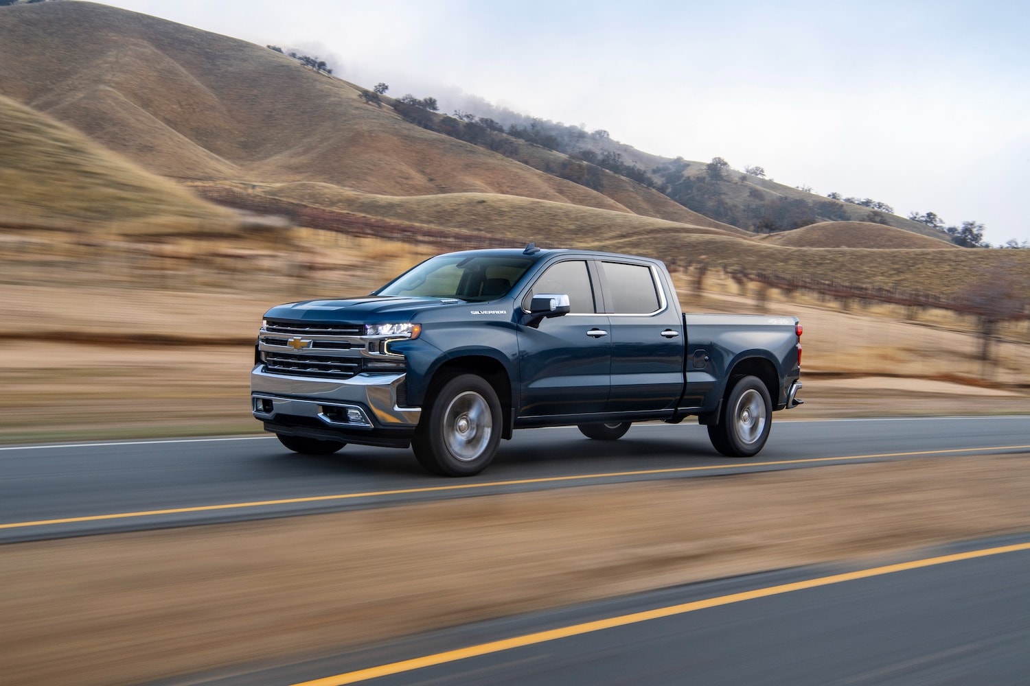 Blue Chevy Silverado 1500 driving down a road.jpeg