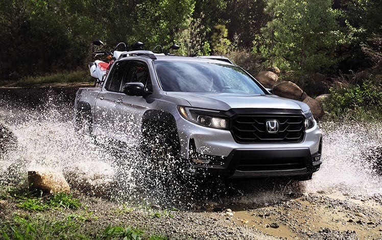 A silver 2023 Honda Ridgeline driving across a shallow river