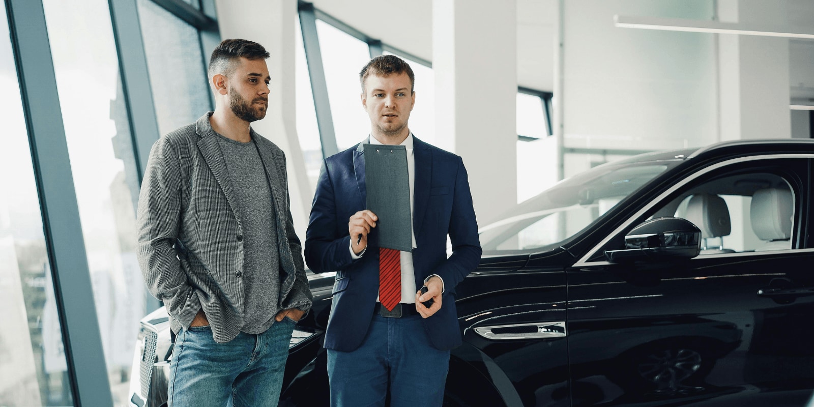 Car salesperson holding a clipboard speaking with a customer about affordable financing inside a dealership