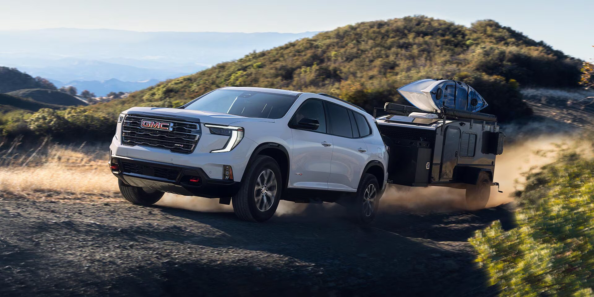 A white gmc acadia driving off-road with a trailer.