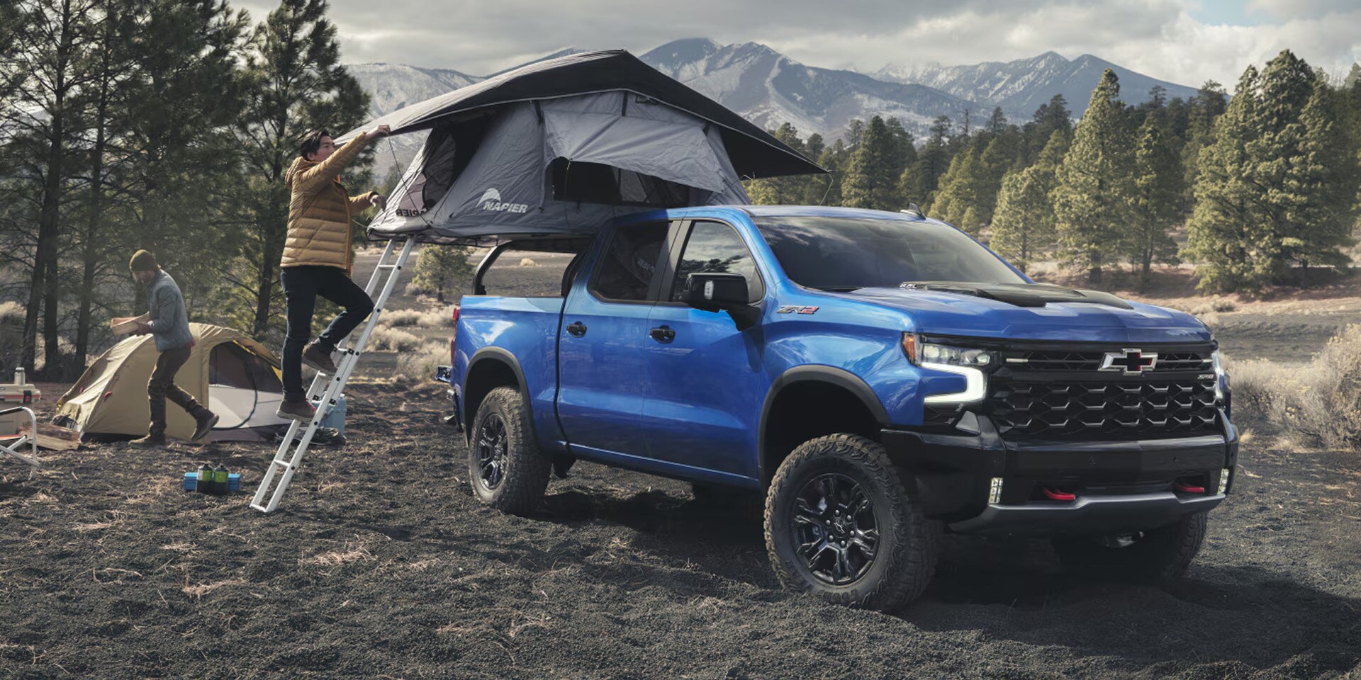 A man setting up a tent on the top of a chevy silverado 1500.