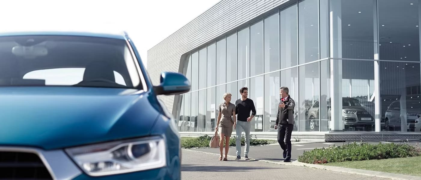 Vue avant de près d'un concessionnaire Audi et d'un préposé au service expliquant la garanti à un jeune couple