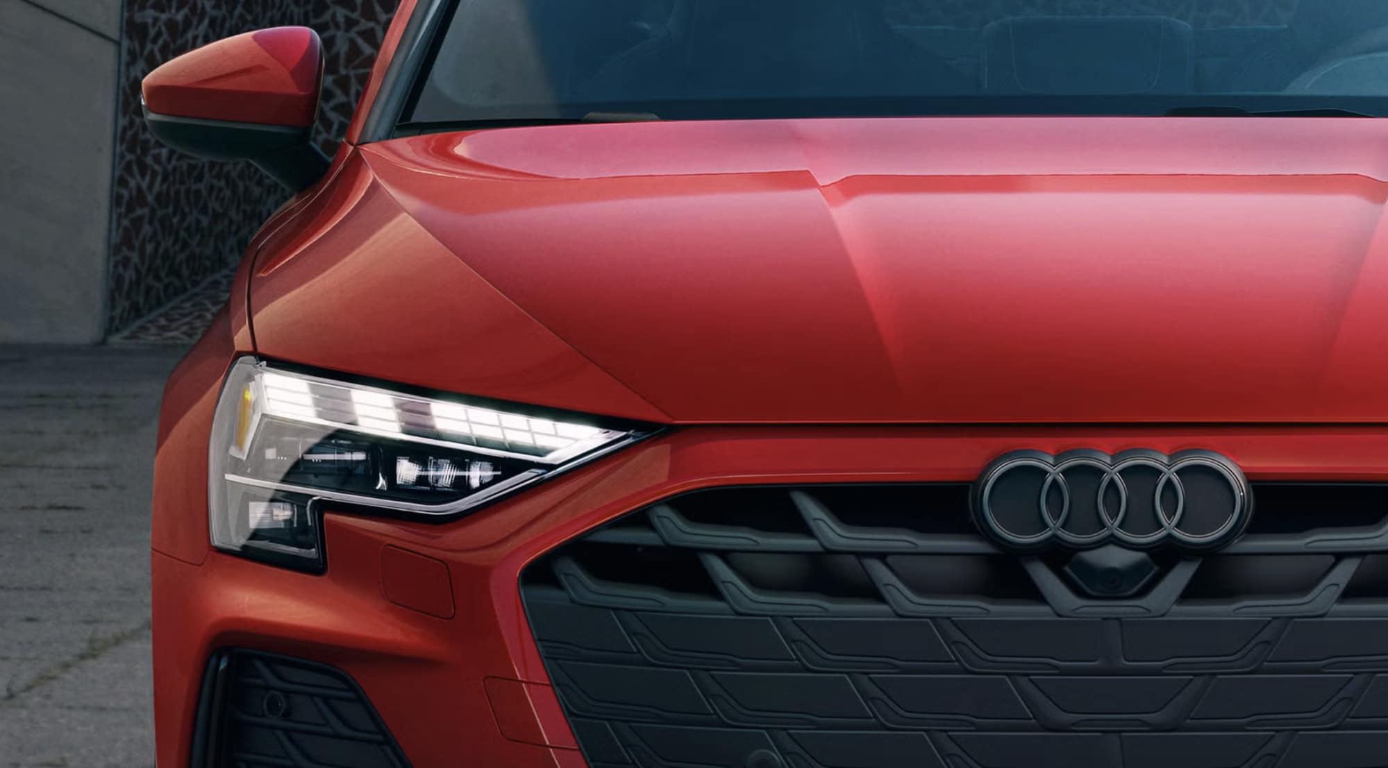 Close-up of the 2026 Audi A3 in Progressive Red showing its LED headlight and Singleframe grille