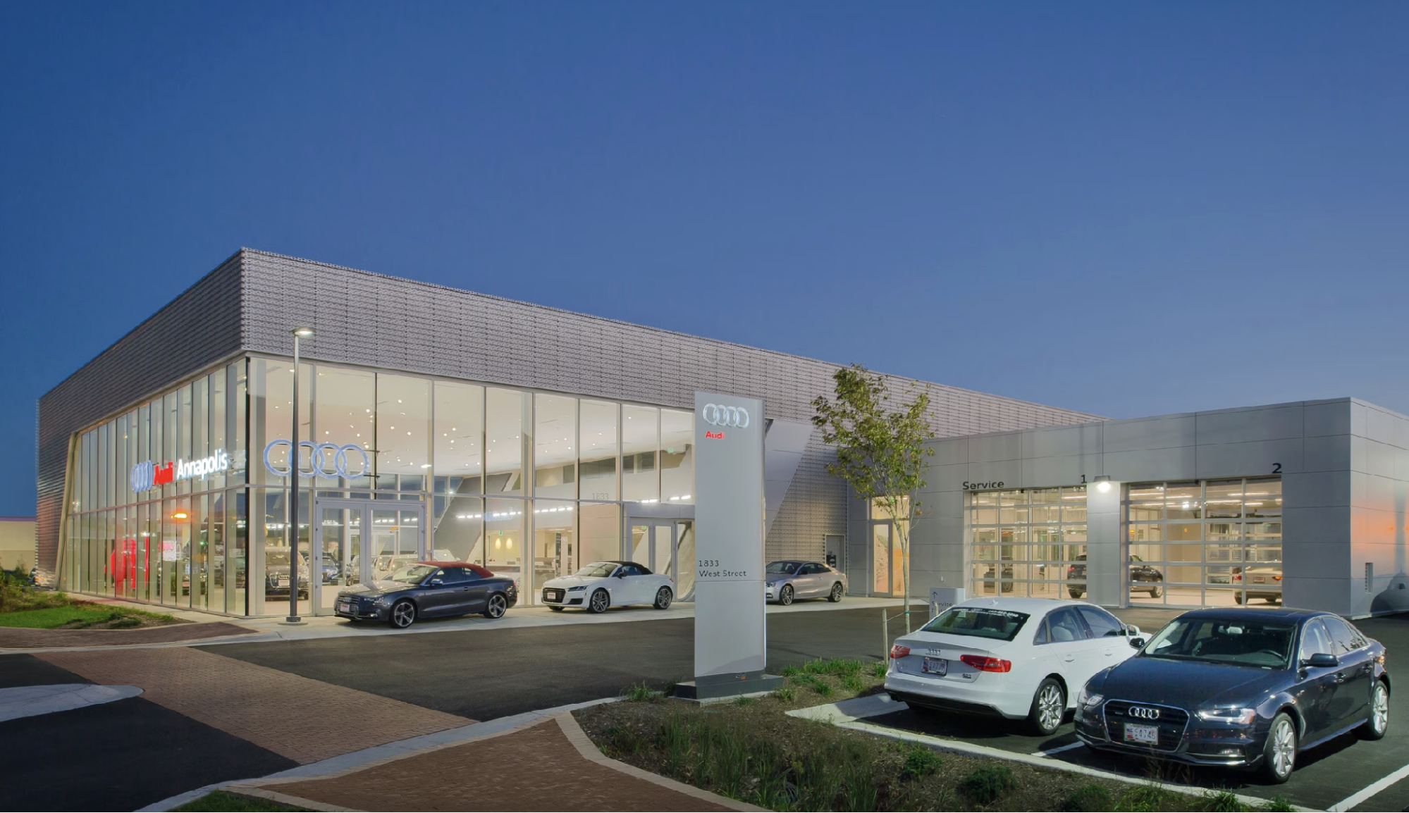Audi Annapolis dealership at dusk with a glass showroom, service bays, and Audi vehicles parked out front
