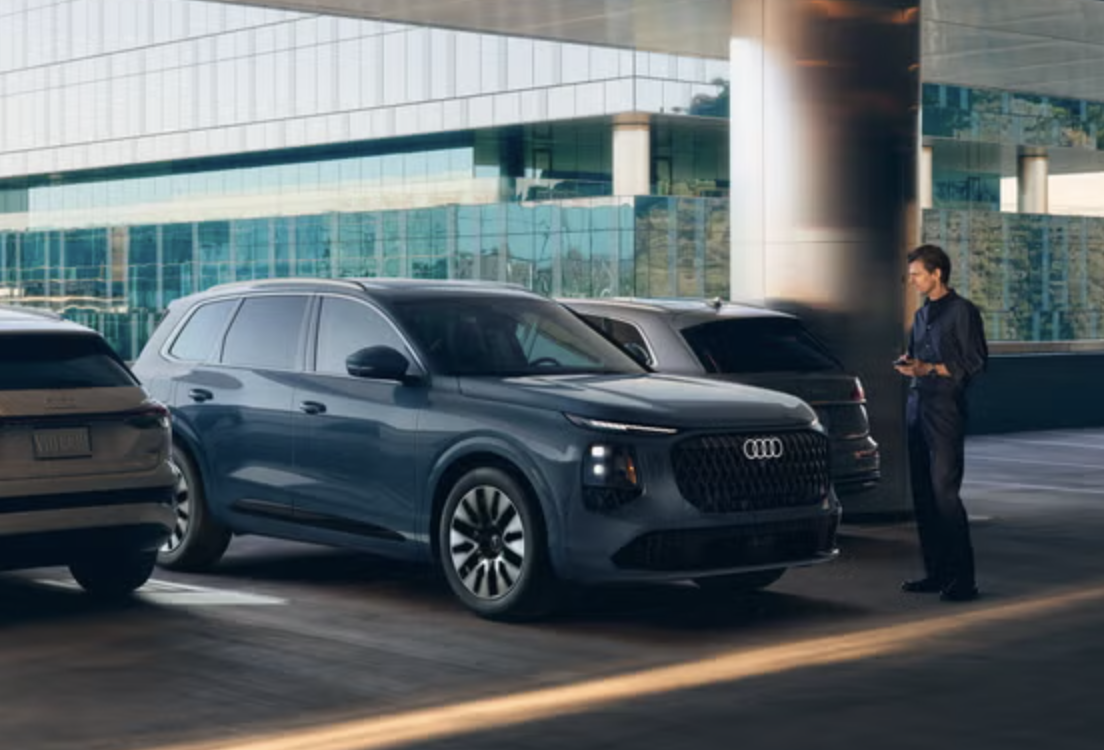 Man using a smartphone to remote park a 2027 Audi Q7 in a parking garage