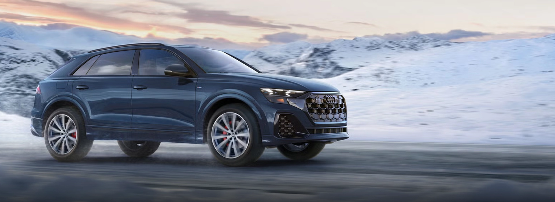 2027 Audi Q8 in dark blue, shown from the front three-quarter angle on a snow-covered mountain road