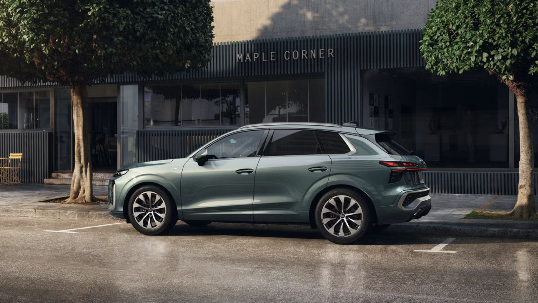 2026 Audi Q3 in a Sage Green parked on a wet city street, showing its sleek side profile and large alloy wheels
