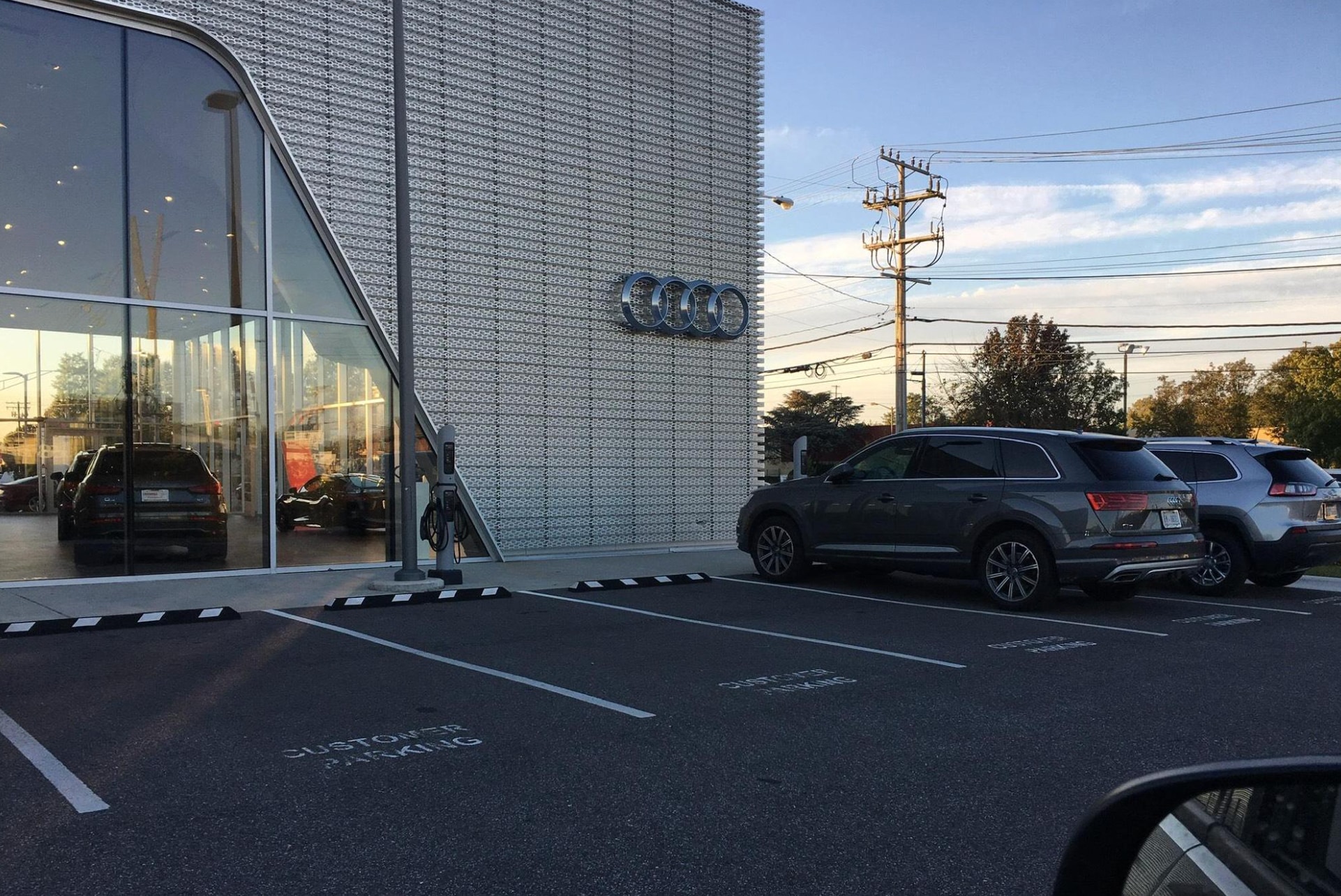 Exterior of the Audi Annapolis dealership with its silver Audi rings logo, glass showroom, EV charger, and customer parking spaces