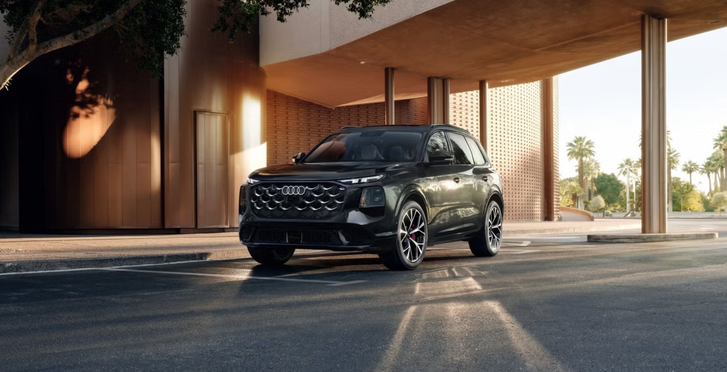 Audi SUV with a bold honeycomb grille parked under a modern building overhang, with palm trees in the background