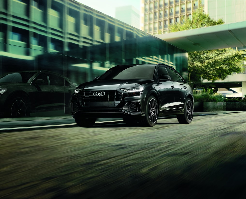 black Audi Q8 luxury SUV driving past a wall of windows on a building