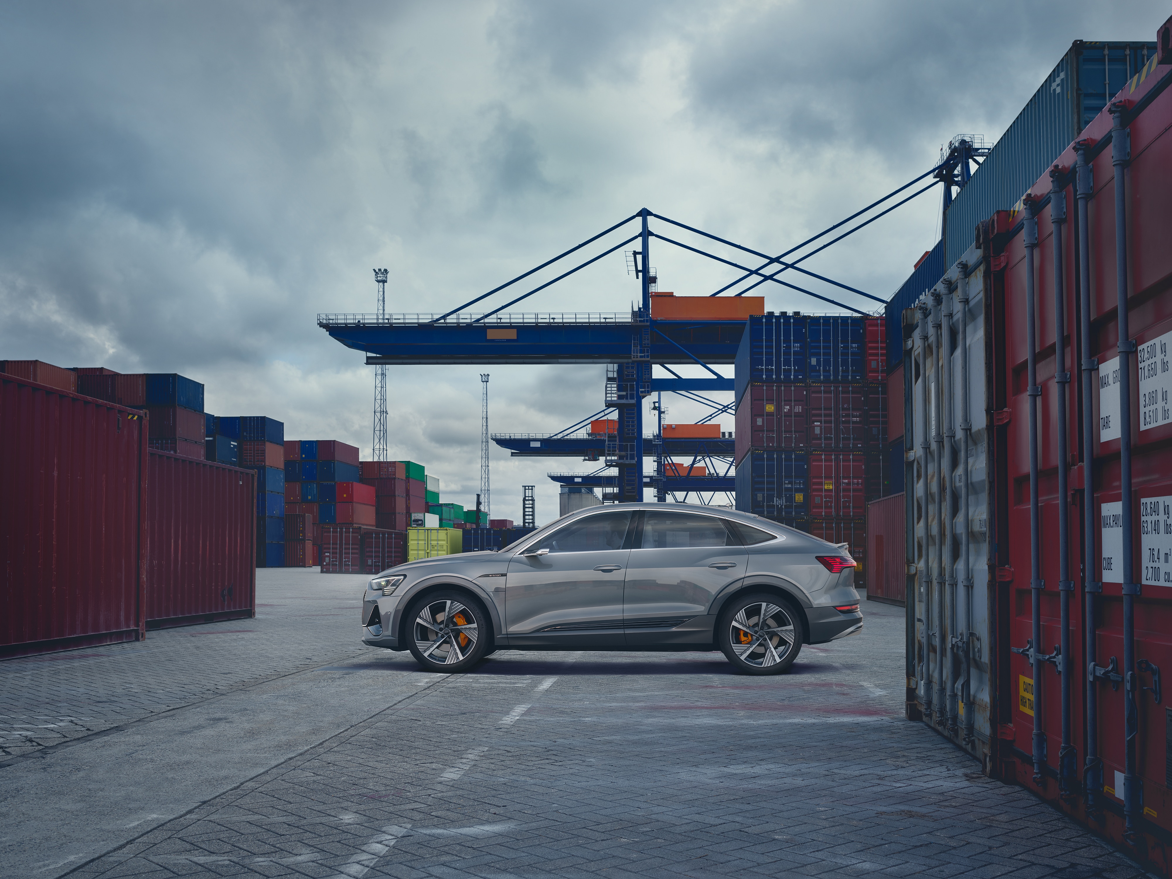 gray Audi e-tron electric luxury SUV parked at a loading dock among shipping containers