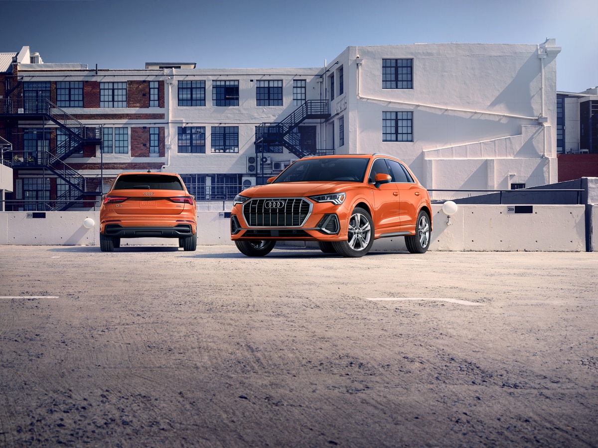 two used orange Audi Q3 SUVs parked on a beach, front and back shown