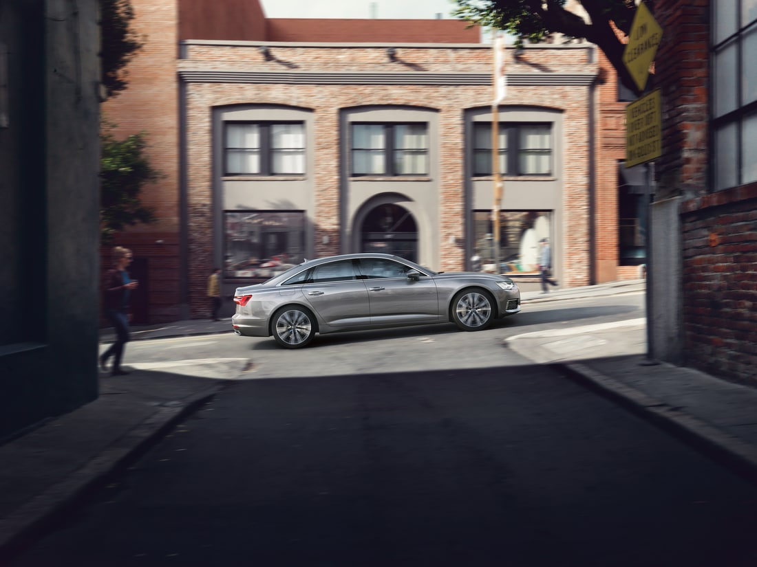 silver Audi A6 sedan driving up hill in a downtown residential area