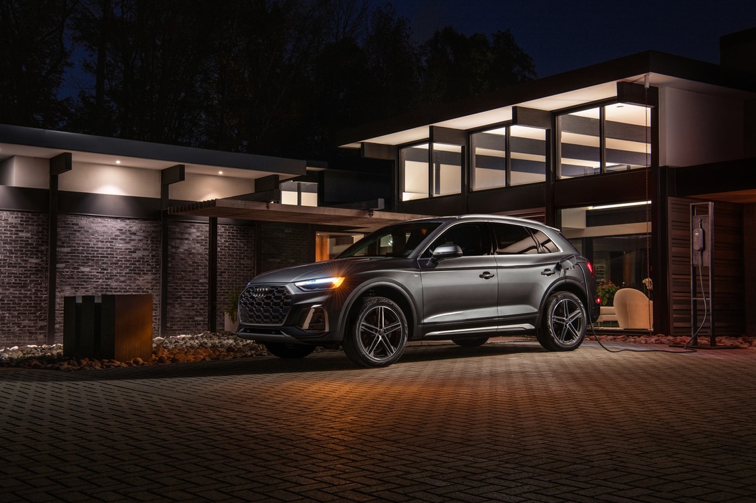 silver Audi Q5e hybrid SUV parked and charging in front of a large, modern garage