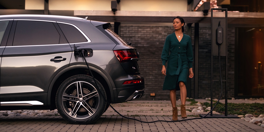 grey Audi Q5e hybrid SUV charging, with the driver walking near the trunk