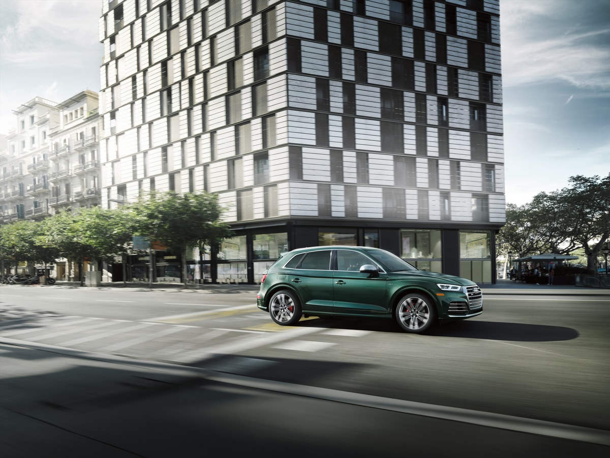 green Audi SQ5 Premium Plus SUV driving past a modern city building