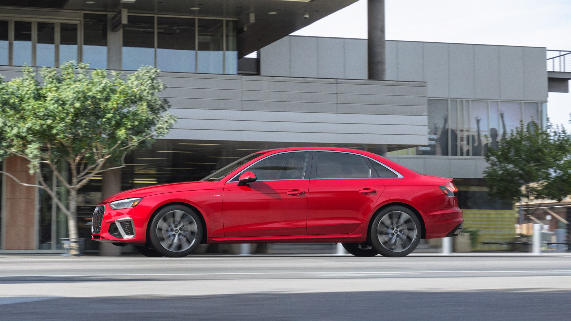 red Audi A4 sedan driving past a modern office building